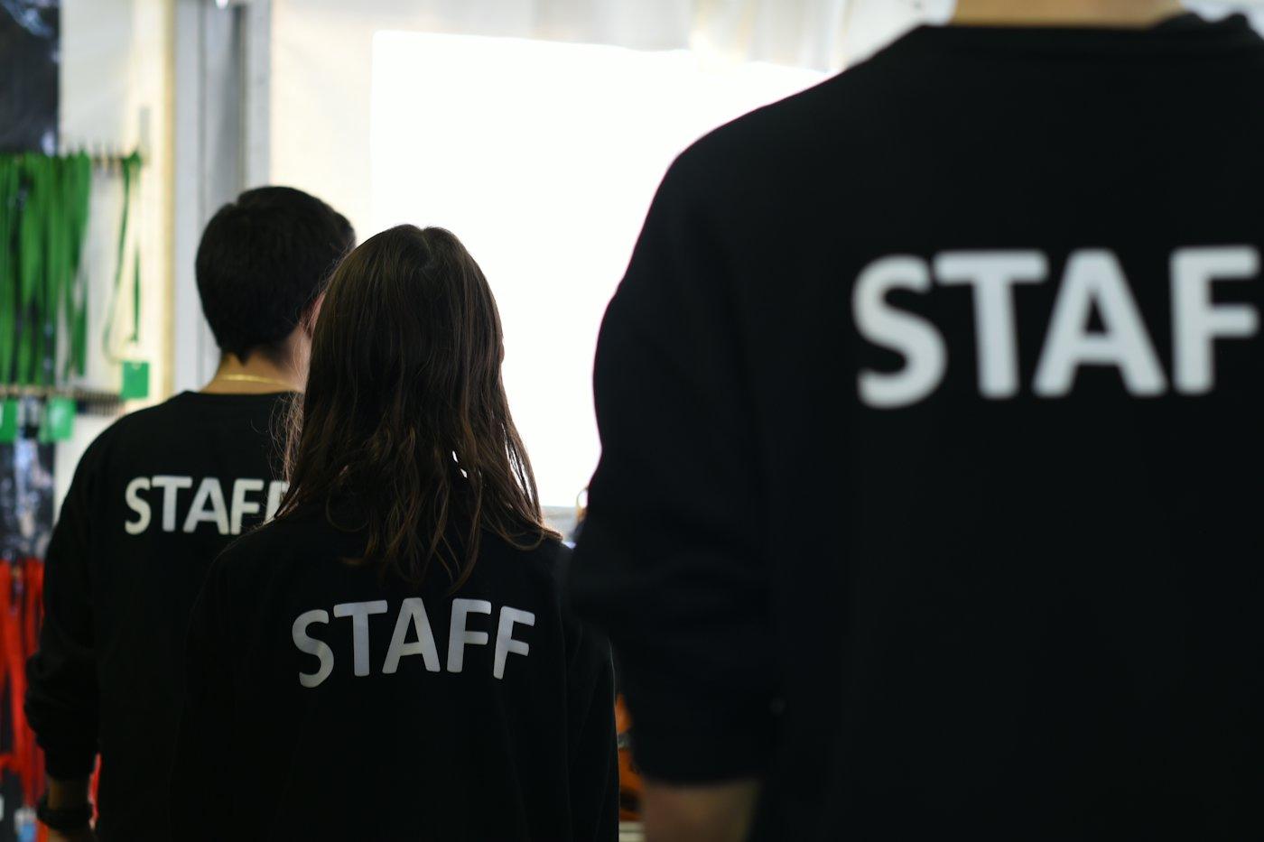 Equipe uniformizada de costas, com a palavra staff nas camisetas